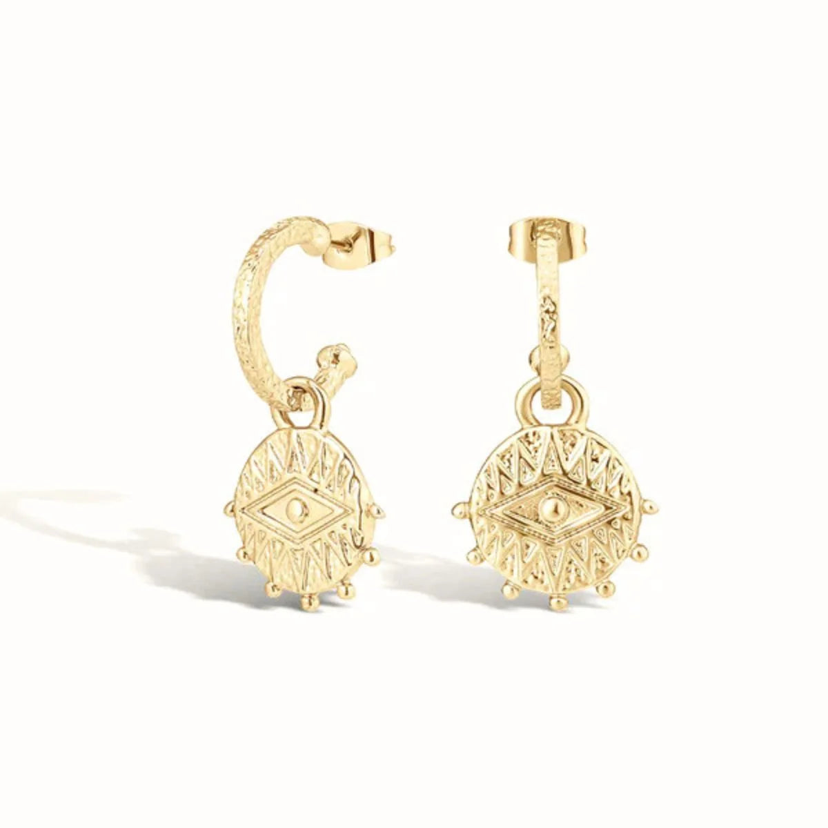 A pair of gold huggie hoop earrings with dangling circular medallion charms featuring an eye motif, shown on a clean white background.