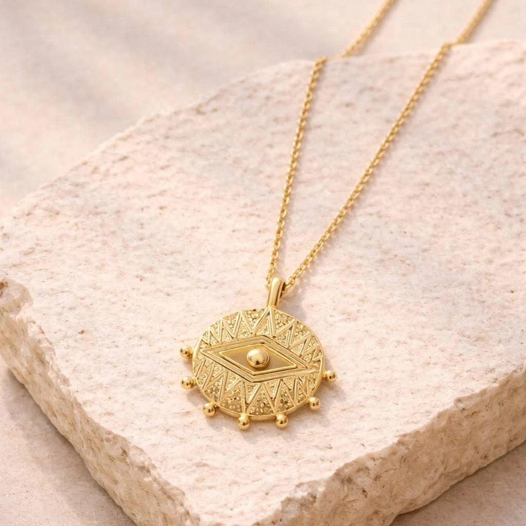 Gold necklace with a decorative eye pendant on a textured beige surface