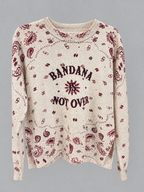 A cream-colored knit sweater with a maroon paisley pattern and the text 'BANDANA NOT OVER' printed on the front, displayed against a solid gray background.