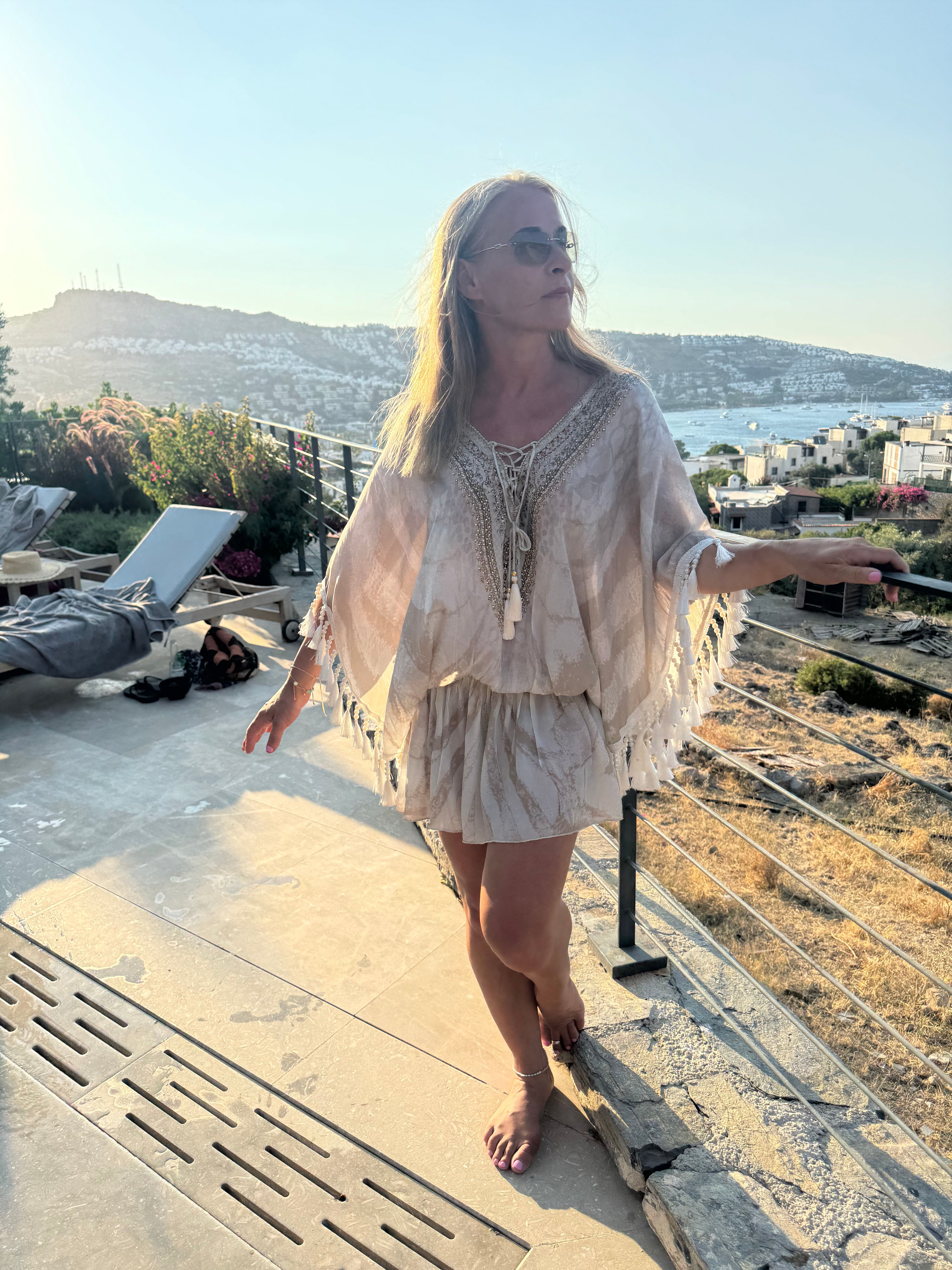 Cream holiday kaftan with a gold sequin V-neck, flowing batwing sleeves, tonal animal print and tassel fringe.