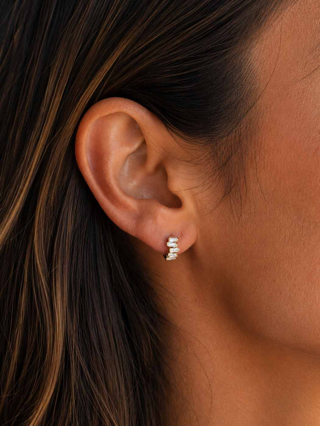 A close-up of a woman's ear wearing a small silver stud earring with baguette style stones