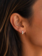 A close-up of a woman's ear wearing a small silver stud earring with baguette style stones