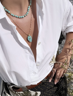Gold chain necklace with a turquoise Hamsa hand pendant and gold evil eye detail, styled with turquoise beads