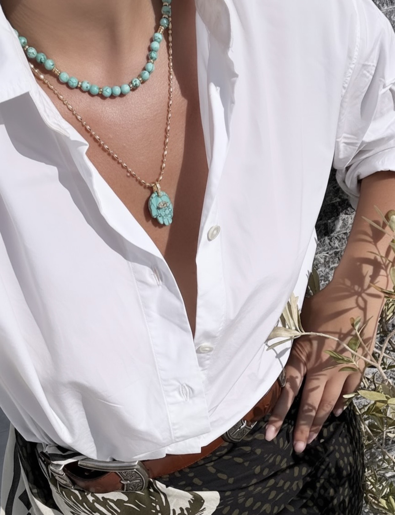 Gold chain necklace with a turquoise Hamsa hand pendant and gold evil eye detail, styled with turquoise beads